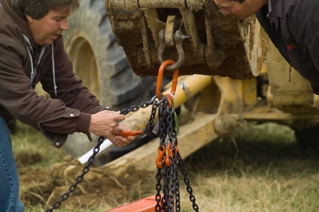 Prevención de riesgos laborales en excavaciones: trabajadores asegurando cadenas para izar caja de zanja.